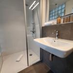 Dusche mit Duschbrause und Spiegel über Waschbecken.