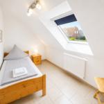 Ein Schlafzimmer mit Dachfenster, Bett, Nachttisch und Stuhl.