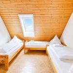 Dreibettzimmer mit Holzdach, Dachfenster und weißen Bettwäschen.