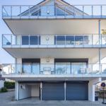 Moderne Villa mit drei Balkonen und Garage. Glasgeländer und großzügige Fenster.
