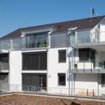 Moderne weiße Villa mit Balkonen und großen Fenstern. Dachterrasse mit Sichtschutz.