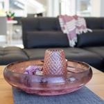 Ein dunkler Sofa im Hintergrund. Auf dem Tisch steht eine rosa Schale mit Deko.