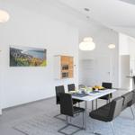 Esszimmer mit Tisch, Stühlen und Küchenbereich. Wandbild und Holzschränke sind sichtbar.