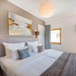 Schlafzimmer mit Bett, Wandbild, Deckenleuchte und TV. Fenster mit Vorhängen.