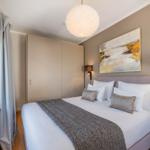 Schlafzimmer mit Bett, Wandbild und Deckenleuchte. Fenster mit Vorhang und Nachttisch.