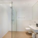 Badezimmer mit Dusche, Waschbecken und Toilette. Weiße Fliesen und moderne Einrichtung.