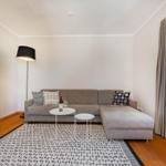 Wohnzimmer mit grauem Sofa, weißen Tischen und Holzboden.
