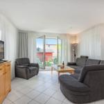 Wohnzimmer mit Sofa, Sessel, TV und Balkonzugang.