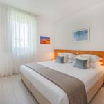 Schlafzimmer mit Doppelbett, Holzfußboden und Fenster mit weißen Vorhängen.