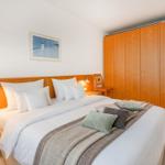 Schlafzimmer mit Doppelbett, Holzschrank und Nachttisch. Wandbild über dem Bett.