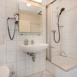 Badezimmer mit Dusche, Waschbecken und Toilette. Wandtrockner und Spiegel sind vorhanden.