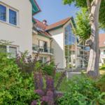 Haus mit Balkon, großen Fenstern und grüner Umgebung