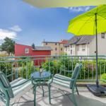 Terrasse mit Tisch, zwei Stühlen und grünem Sonnenschirm. Blick auf Wohnhäuser und Grünflächen.