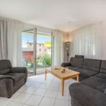 Wohnzimmer mit grauem Sofa, Tisch und Balkon. Helle Wand, weiße Fliesen.