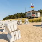 Strand mit weißen Liegestühlen und Strandhaus im Hintergrund.