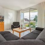 Wohnzimmer mit Sofa, Couchtisch und Fernseher. Durchgang zur Terrasse mit Blick auf Dächer.