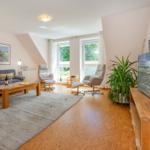 Wohnzimmer mit Sofa, zwei Sesseln, TV und Fenster mit Blick auf Grün.
