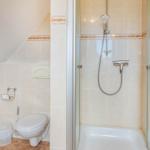 Bad mit Dusche, Toilette und Toilettenpapierhalter an der Wand.