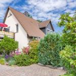 Haus mit Balkon, rotem Sonnenschirm und blühendem Garten unter blauem Himmel.