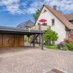 Haus mit Terrasse, rotem Sonnenschirm und gepflasterter Hof. Garten mit Blumen und Bäumen.