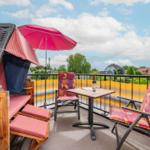 Terrasse mit Sonnenschirm, Tisch und Stühlen. Blick auf Wohngebiet und Bäume.