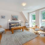 Wohnzimmer mit Sofa, Sesseln und Fenstern. Holzfußboden und Teppichboden.
