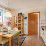 Esszimmer mit Tisch, Stühlen und Küchenbereich. Fenster mit Blick auf Garten.