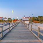 Holzbrücke führt zum Strand und zu Hotels mit roten Dächern.