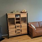Holzschrank mit Glasfronten, Radio und dekorativen Gegenständen neben einem braunen Sofa.
