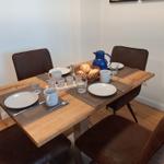 Esszimmer mit Holztisch, vier Stühlen und Frühstücksgeschirr.