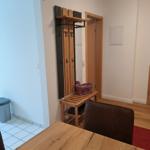Eingangsbereich mit Holzgarderobe, Stuhl und Tisch. Flur mit Tür und Wandkasten.