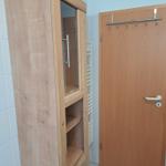 Hölzerner Schrank mit Glasfront und Schubladen neben einer Tür mit Haken.