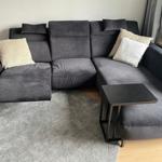Ein grauer Ecksofa mit Kissen und zwei kleinen Tischen auf Teppich und Holzfußboden.
