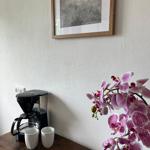 Eine Kaffeemaschine mit zwei Tassen auf einem Holztisch neben einer Orchidee und einem Bild an der Wand.