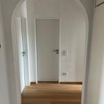 Höhenbogen führt in einen Flur mit Holzboden und weißen Türen.
