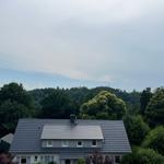 Haus mit grauem Dach und Fenstern, umgeben von Bäumen und Wald.