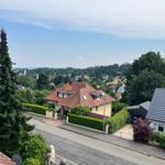 Haus mit rotem Dach und grüner Hecke. Blick auf die Straße und umliegende Häuser.
