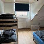Zimmer mit Doppelstockbett, Einzelbett, Fenster und Heizung.