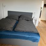 Doppelbett mit grauer Bettwäsche und blauer Matratzenhülle.