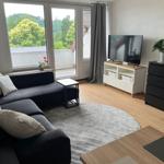 Wohnzimmer mit Sofa, TV und Balkonblick. Holzboden und graue Teppiche.