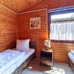 Zimmer mit zwei Betten, Holzwand und Fenster mit Vorhang.