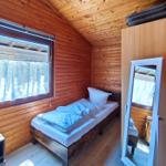 Ein Schlafzimmer mit Holzwand, Bett, Spiegel und Fenster mit Vorhang.