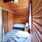 Zimmer mit Holzwand, zwei Betten und Nachttisch mit Lampe.