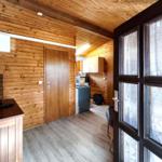 Wohnraum mit Holzwand, Fernseher und Tür zum Flur. Durchgang zu Küche und Wohnbereich.