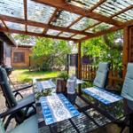 Terrasse mit Tisch, Stühlen und Grill unter Holzüberdachung mit Glasplatten.