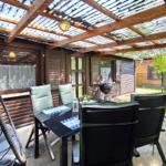 Terrasse mit Sitzgruppe, Grill und Holzüberdachung. Hinterhof mit Grünflächen.