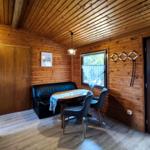 Wohnraum mit Holzwand, Tisch, Sofa und Fenster mit Gardine.