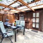 Terrasse mit Tisch, Stühlen und Hängesessel unter Holzüberdachung.