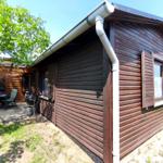 Holzhütte mit Terrasse, Grill und Sitzgelegenheiten unter Bäumen.