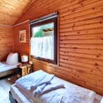 Zwei Betten in einem Holzhauszimmer mit Fenster und Nachttisch.